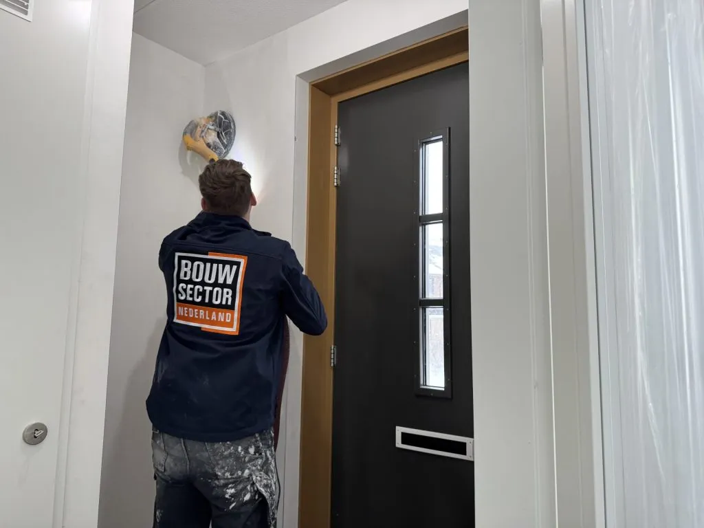 Medewerker van Bouwsector Nederland schuurt met een schuurgiraffe de wand van een hal in een nieuwbouwwoning