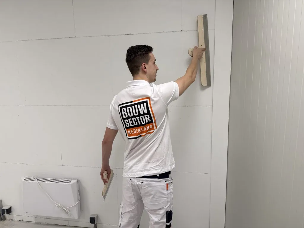 Stukadoor van Bouwsector Nederland werkt een wand af met een vlakspaan en een plamuurmes