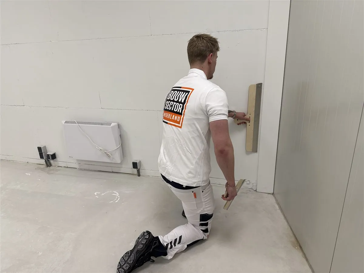 Stukadoor Bram van Bouwsector Nederland werkt geknield met een spaan langs een wand van gipsblokken