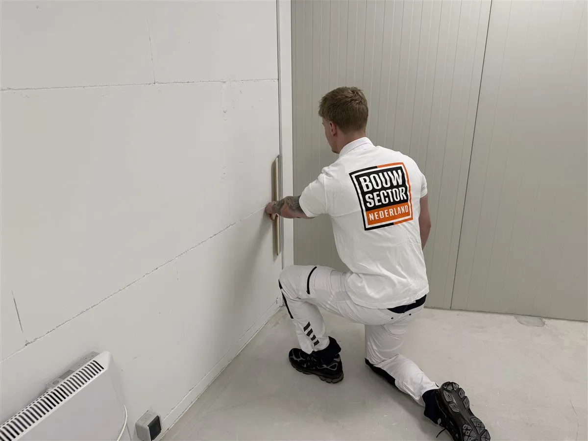 Stukadoor Bram van Bouwsector Nederland zet in een hoek een spaan tegen de wand