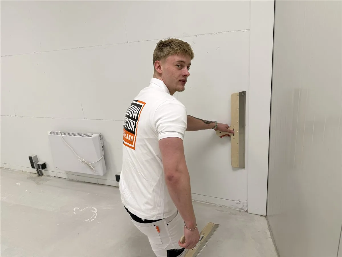 Stukadoor Bram van Bouwsector Nederland kijkt om terwijl hij een spaan tegen de wand houdt