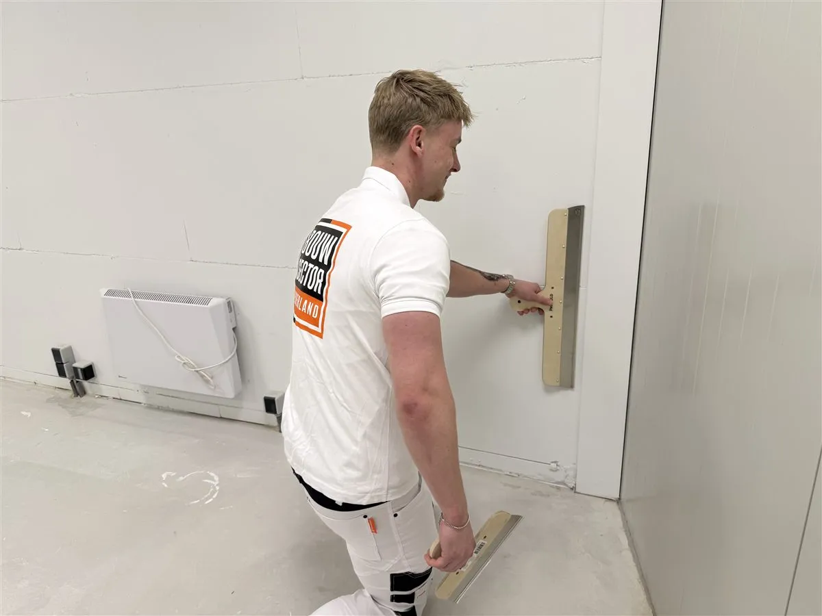 Stukadoor Bram van Bouwsector Nederland strijkt met een spaan over een witte wand