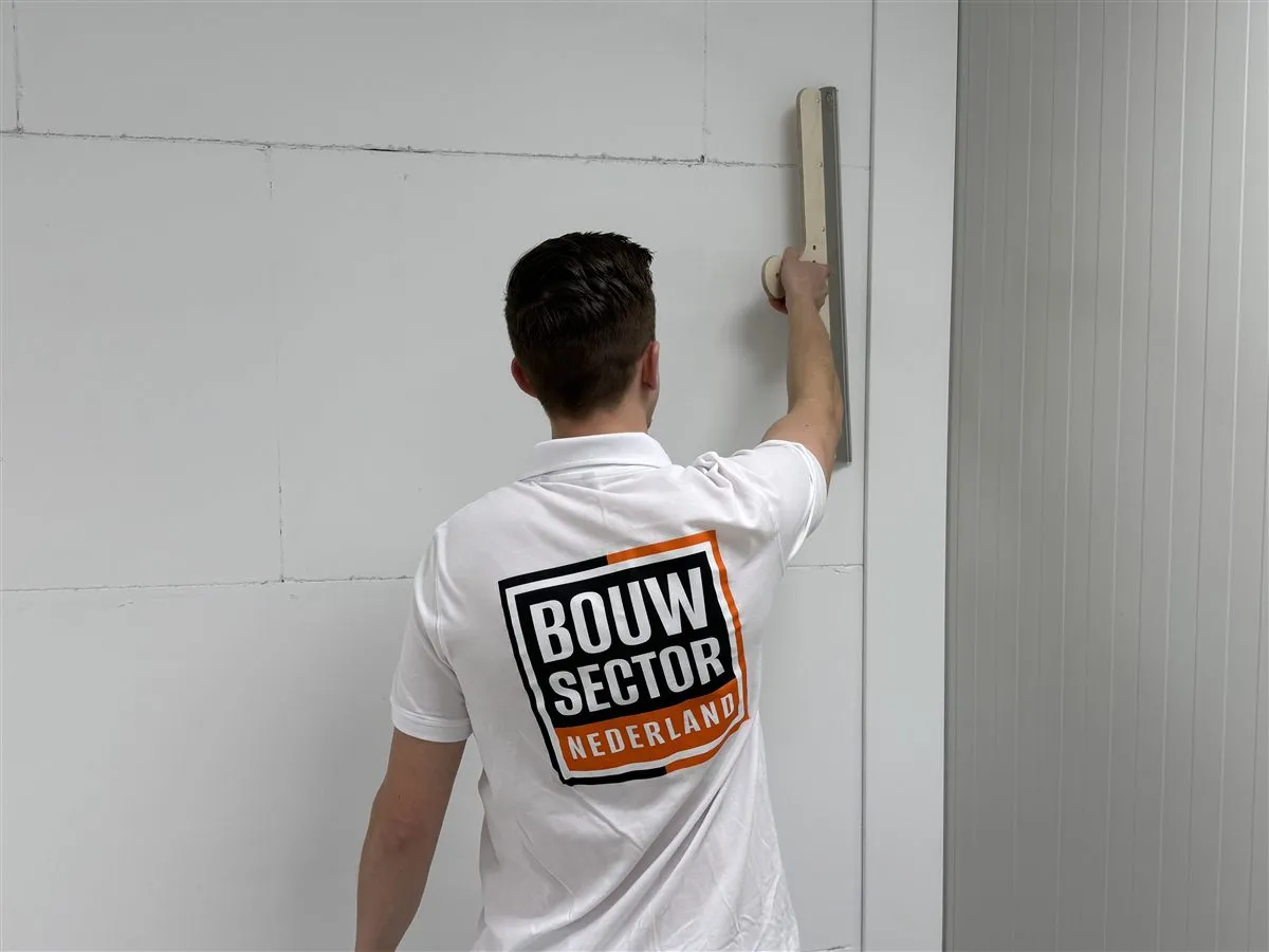 Vakman Argi van Bouwsector Nederland drukt een spaan tegen een wand van gipsblokken