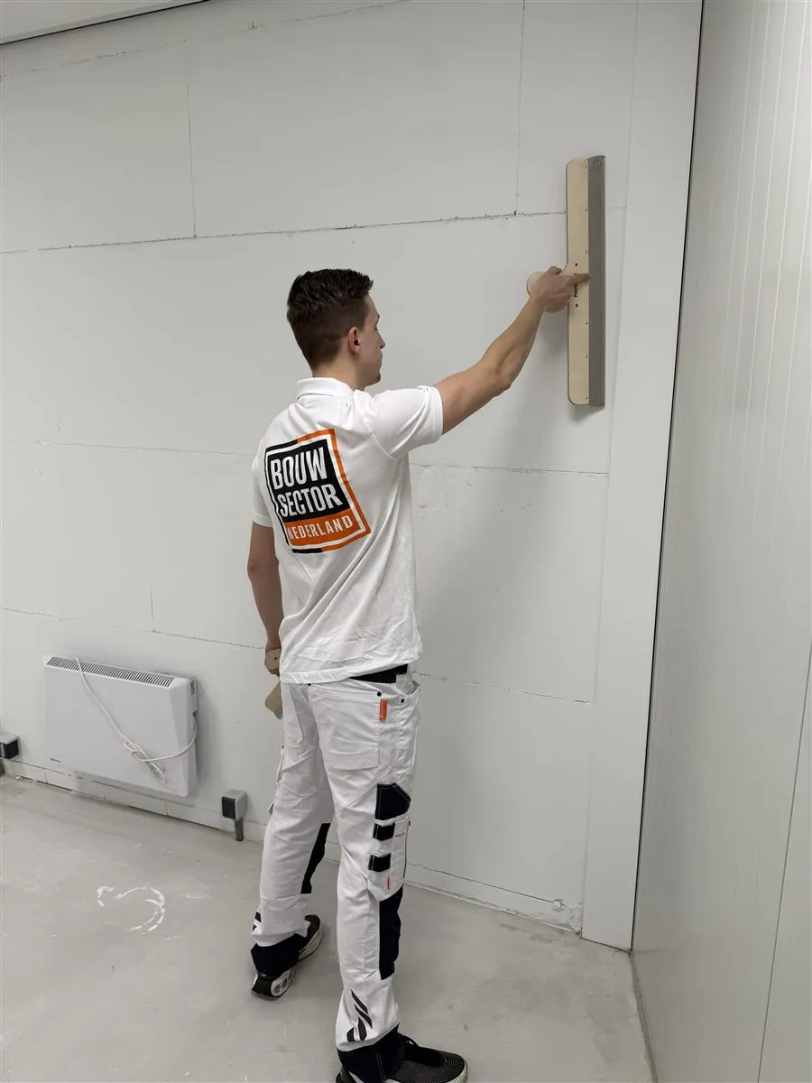 Vakman Argi van Bouwsector Nederland staat met een spaan aan de wand in een lege ruimte