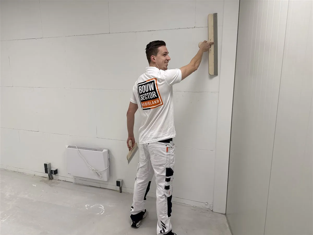 Vakman Argi van Bouwsector Nederland werkt met twee spanen aan een wand