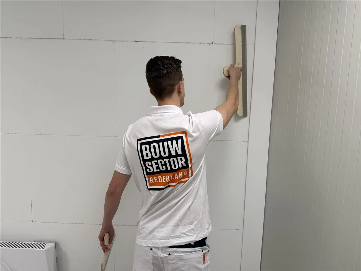 Vakman Argi van Bouwsector Nederland strijkt met een spaan over een wand van gipsblokken