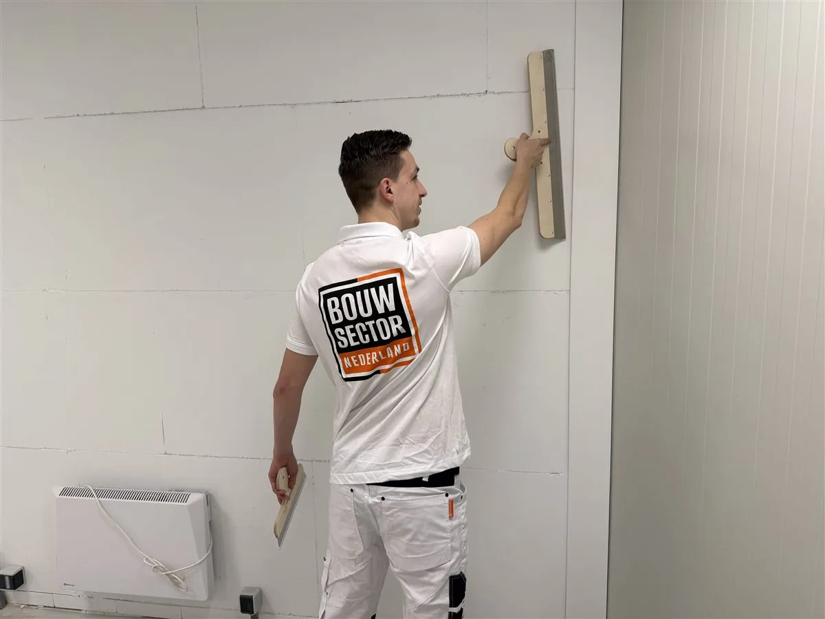 Vakman Argi van Bouwsector Nederland zet een spaan tegen de wand boven een radiator