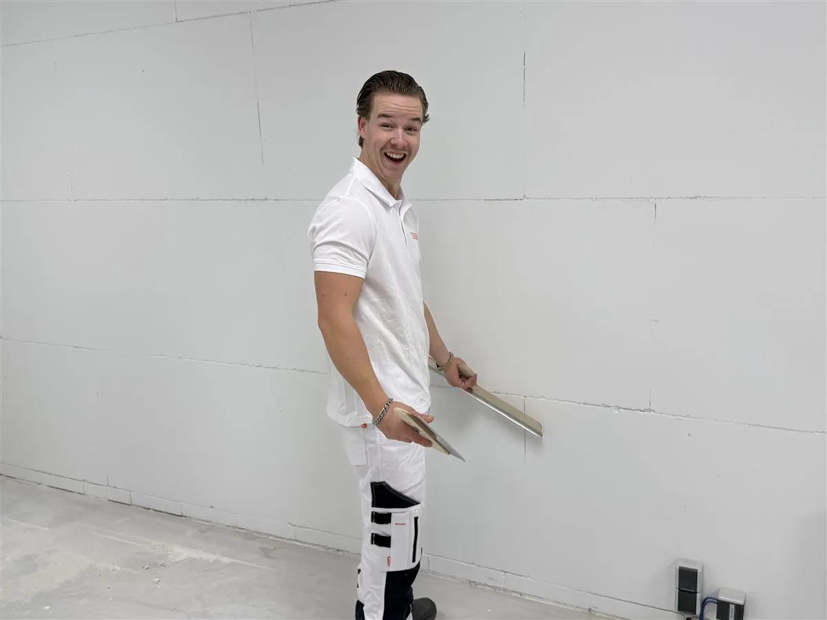 Lachende vakman Chris van Bouwsector Nederland met een spaan voor een wand van gipsblokken
