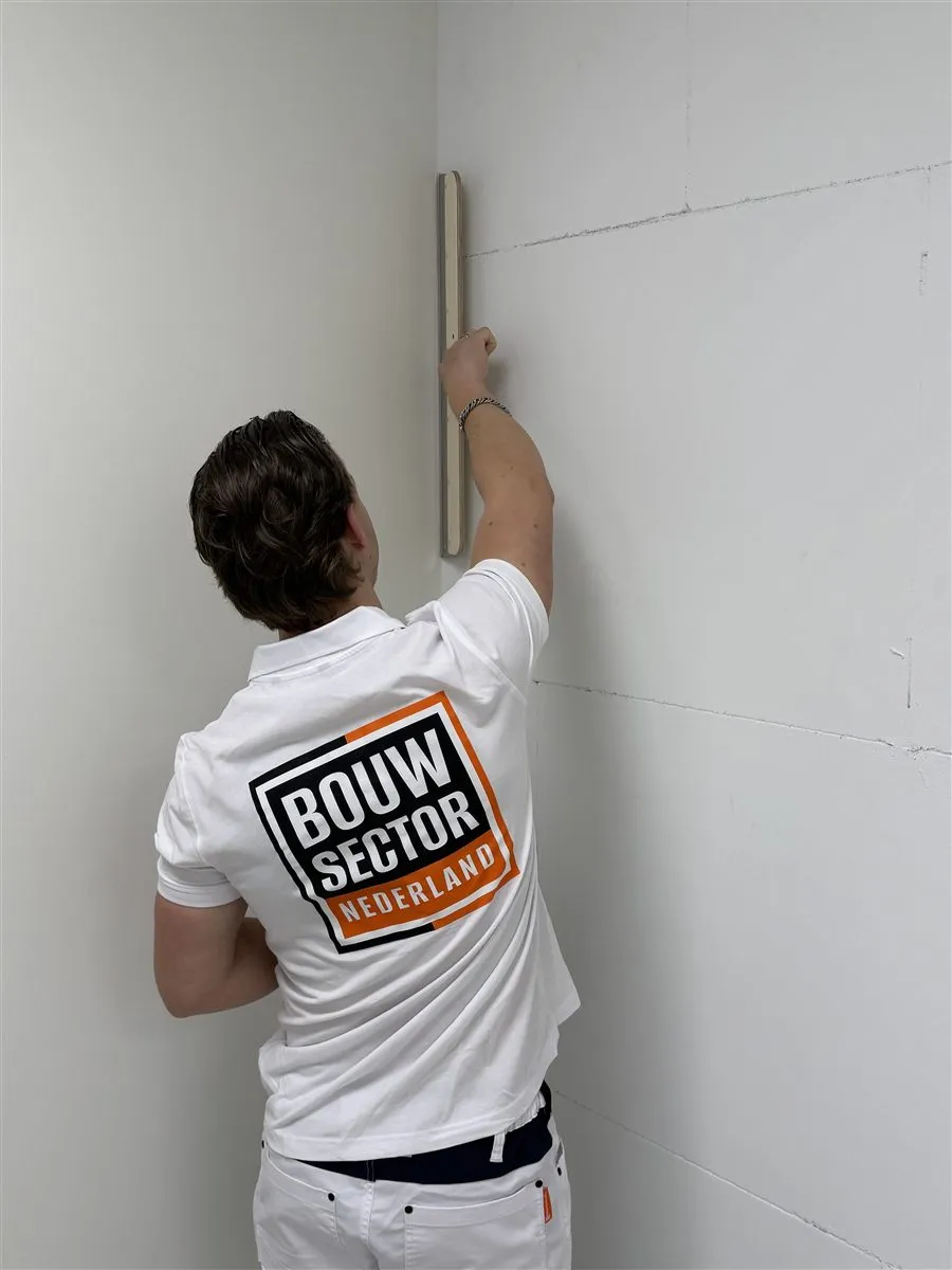 Vakman Chris van Bouwsector Nederland zet een lange spaan hoog in de hoek van de wand