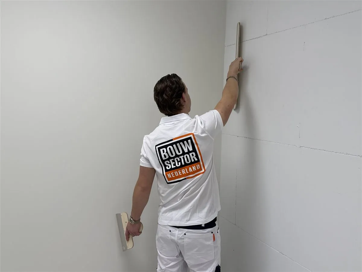 Vakman Chris van Bouwsector Nederland werkt met een lange spaan boven zijn hoofd aan de wand